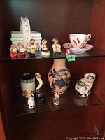 Top shelf showing four small figurines and ceramic basket with a tea cup and saucer