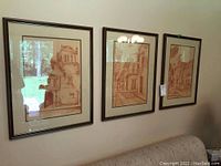 Three sepia-tone framed prints on a wall above a couch. Architectural scenes are depicted.