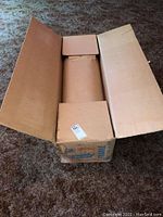 Photo of the large sandpaper roll inside an open cardboard box resting on carpeted floor.