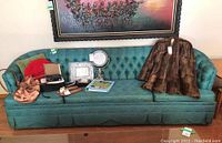Front view of vintage teal button-tufted sofa with skirt and various items on seat, showing upholstery texture and condition.