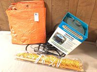 Lot contents shown: orange tarp folded, yellow hammock rope coiled with plastic wrapping, and boxed Bite Shield Mosquito Trap Protector device with power cord visible.