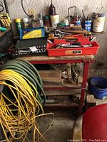 Overview of the top of the red metal cart with tool boxes, assorted hand tools, and cans of lubricants and oils in the background.