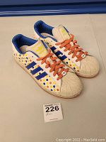 Pair of Adidas polka dot sneakers side view showing white leather base with multicolored dots, blue stripes, and orange laces