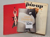 Front view of three books stacked showing covers including '1000 Dessous' on top and 'The Pin-up' beneath
