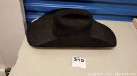Side and front view of the black cowboy hat on a table with a blue background.