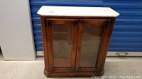 Front view of wood display cabinet with glass doors and marble top.