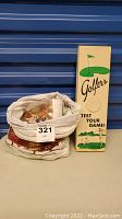 Golf balls and tees stored in a cloth bag alongside a vintage Golfers Test Your Game potentiometer box.