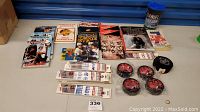 Overview of collection showing multiple Vancouver Canucks yearbooks, Don Cherry's Hockey Stories, The Mick book, team hockey pencil packages, O-Pee-Chee bubble gum trading card package, four new pucks with photos sealed in plastic, and Daniel Sedin plastic cup.