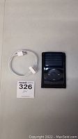 Apple iPod Classic with dock connector cable and auction tag on table.
