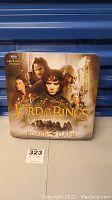Front view of the Lord of the Rings board game in a tin box featuring main character artwork and title text.