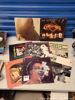 Overall view of 12 vinyl record albums arranged on a table including artists such as Isaac Hayes, Commodores, Billie Holiday, Scott Joplin, and more.