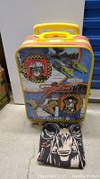 Front and side view of Star Wars themed rolling bag with yellow handle and retractable pull handle, showing character and spacecraft graphics on the bag surface