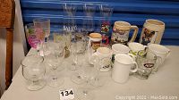 Full view of all glassware and mugs on table including stemmed glasses, steins, A&W mug, Starbucks cup, and others