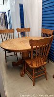 Wooden oval dining table with four matching chairs around it, all wood with carved details and natural finish.