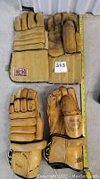 Top-down view of both pairs of vintage hockey gloves side by side highlighting leather wear and label patch on one pair