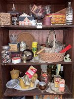 Three shelves of assorted vintage items including glass bottles, buttons in jars, advertising tins, woven baskets, kitchenware, and small collectibles.