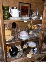 Wide view of cabinet interior showing plates, teapot, glassware, brass candlestick, ceramic figurines, and tools on shelves