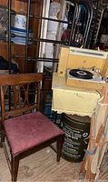 Photo showing full size metal bed components with wood dough box table top, solid wood chair with pink cushion, Civil Defense water container, and record player cabinet.