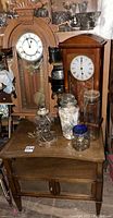 Photo of two wooden clocks, side table with two mesh-covered doors, assorted glass jars including a tall jar with shells, and a converted oil lamp light on top of the side table