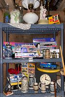 Three shelves filled with collectible boxed trucks, steins, vintage clock, books, and small collectibles as seen in the lot.