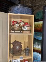 Shelf with ceramic cookie jar, wooden cuckoo clock, metal container, and blue enamel pot on top