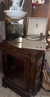 Wood and glass display cabinet with mirror back and glass shelves, pitcher and bowl on top, gold footrest, and vintage record player on top