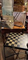 Double sided game table with checkerboard surface on black metal folding base with toolbox, metal magazine rack, and other items on wooden table