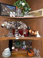 Three wooden shelves filled with a variety of vintage collectibles, ceramic figurines, jars of buttons, decorative glassware, and art pieces.