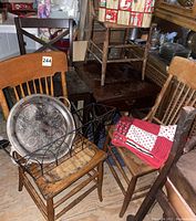 Four assorted worn wooden chairs, dark wooden side table, picnic basket, wire bin, and metal tray displayed on and around chairs indicating condition and details of wear.