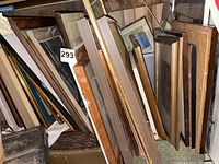 Overall view of large stack of assorted framed artwork and empty frames leaning upright against a wall.