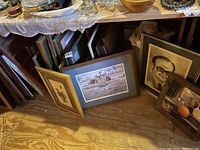 Various framed art pieces leaning and stacked in a corner, including wildlife prints and portraits