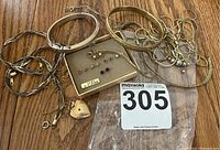 Wide view of assorted gold-filled jewelry including bracelets, chains, and a box of earrings lying on a wood surface with auction lot tag 305.