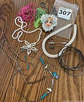 Photo of assorted jewelry including necklaces, a signed face pin with fabric and lace, and hoop earrings.