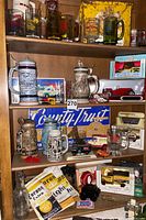 Photo of wooden shelves containing German beer steins, model trucks, fire mugs, vintage signage and memorabilia including Corona and Coca-Cola items.