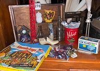 Wide photo of lot on wooden surface showing Lincoln Logs box, assorted bottles, Velvet can, aquarium air pump box, small decorative ceramics and metal items.