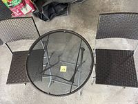 Top view showing round glass top table with grey woven border and two matching folding chairs with woven seats and backs