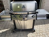 Front view of the Broil King BBQ grill showing the stainless steel body, side shelves, and wheels.