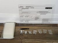 Photo showing the clear Canada Post acrylic sizing guide with printed dimension lines and text labeling various lettermail size limits, calibration weights in small sealed plastic bags, a pen for scale, and a large stack of clear resealable plastic bags.