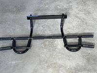 Full view of the black metal chin up bar showing padded foam grips on multiple sections and doorframe hooks.