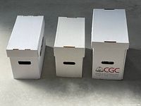 Three white cardboard comic storage boxes of two standard sizes and one large CGC branded box, closed and standing upright