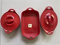 Three red ceramic Corningware casserole dishes including two oval dishes with lids and one rectangular dish without lid shown from top view.