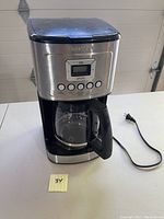 Full view of coffee machine showing stainless steel and black finish, LCD screen, control buttons, and attached carafe on warming plate.