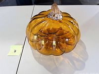 Amber glass pumpkin viewed at an angle showing ribbed texture and clear stem.