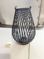 Front angled view showing teardrop-shaped black metal frame and clear glass cylinder inside