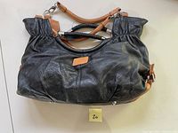 Front view of large black pebble leather handbag with tan leather accents and braided handles, showing gathered top and soft body.