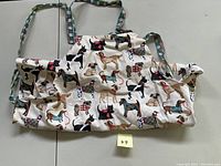 Full view of the dog-print kitchen apron showing the front side with various colored dog illustrations on a white background and plaid straps.