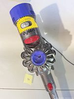 Top view of Dyson V7 Motorhead Origin cordless vacuum unit showing motor and cyclonic system with yellow warning labels and gray/purple coloring.