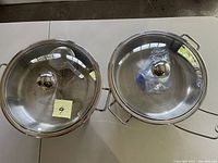 Two stainless steel hot serving bowls with lids seen from above.
