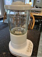 White KitchenAid blender with a clear glass blending jar, shown on a dark granite countertop under daylight near a window.