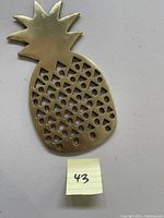 Photo of brass plated pineapple kitchen spoon rest with tag number 43, showing the cut-out pattern on the front.